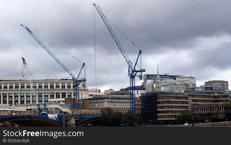 the banks of the thames. on the left side of the river a construction site and its cranes at work.