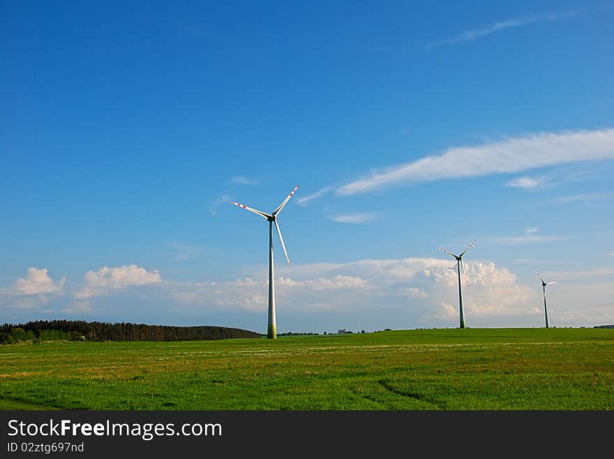 Three windmills standing on a large green field