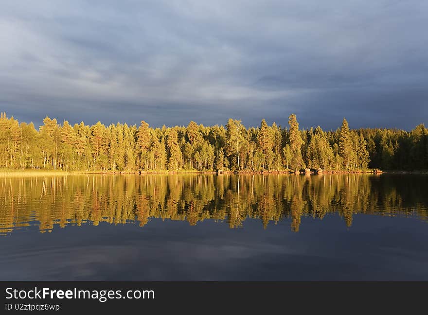 Storm clouds as the sun shines on the forest by a lake. Storm clouds as the sun shines on the forest by a lake.