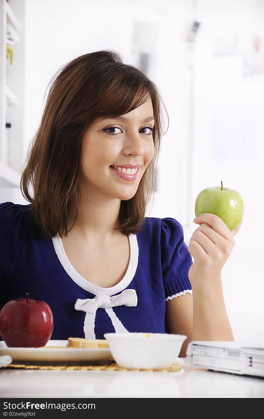 Young woman in breakfast, eating green apple, smiling and looking in camera. Young woman in breakfast, eating green apple, smiling and looking in camera