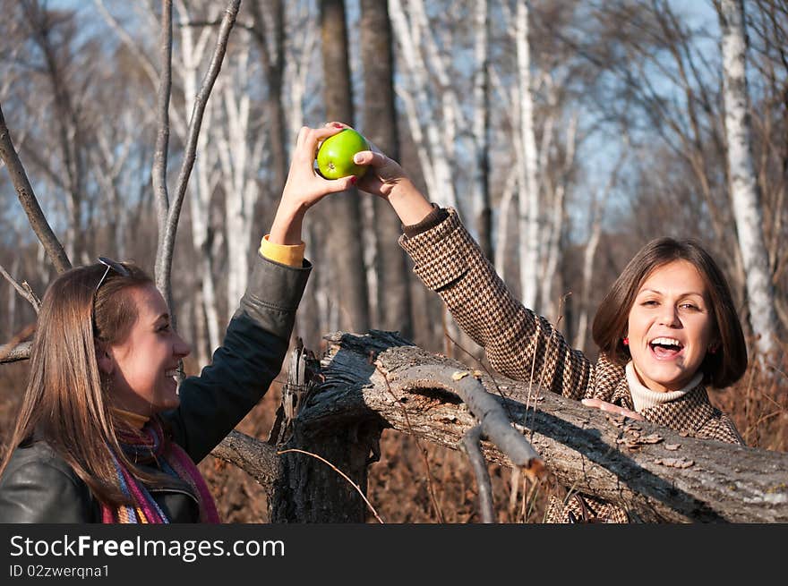 Two young beautiful women playing with green apple in the autumn forest. Two young beautiful women playing with green apple in the autumn forest