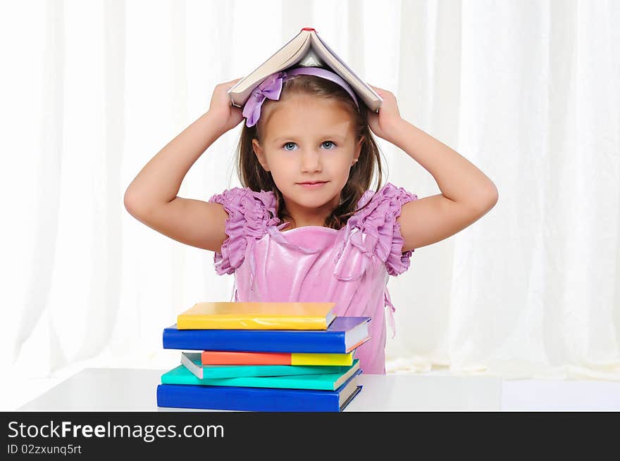 The little girl is studying literature. Reads a book while sitting at a white table.