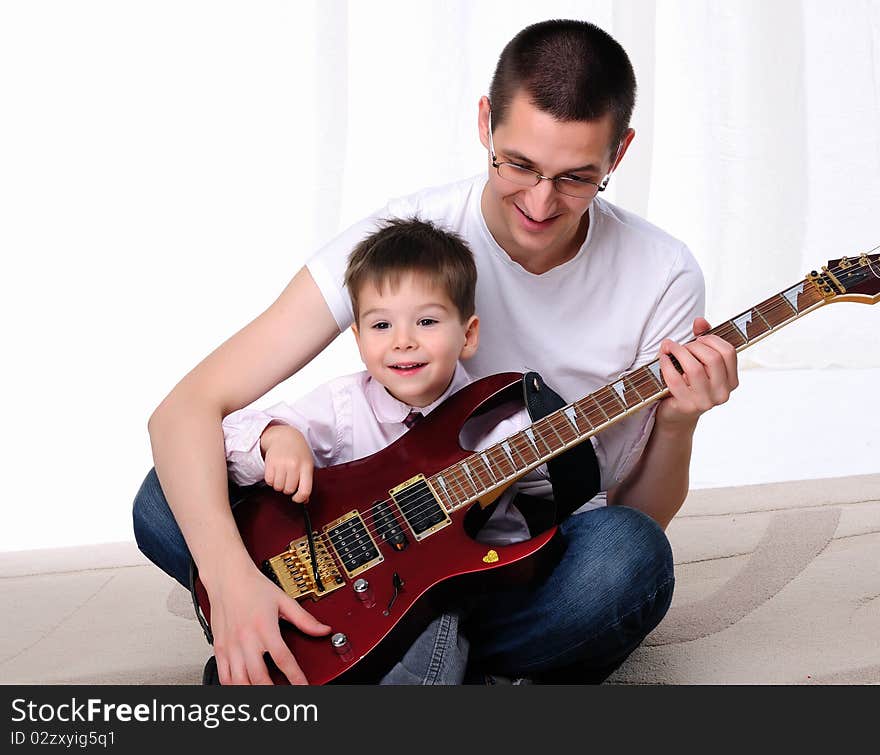 A young father teaches his young son to play guitar