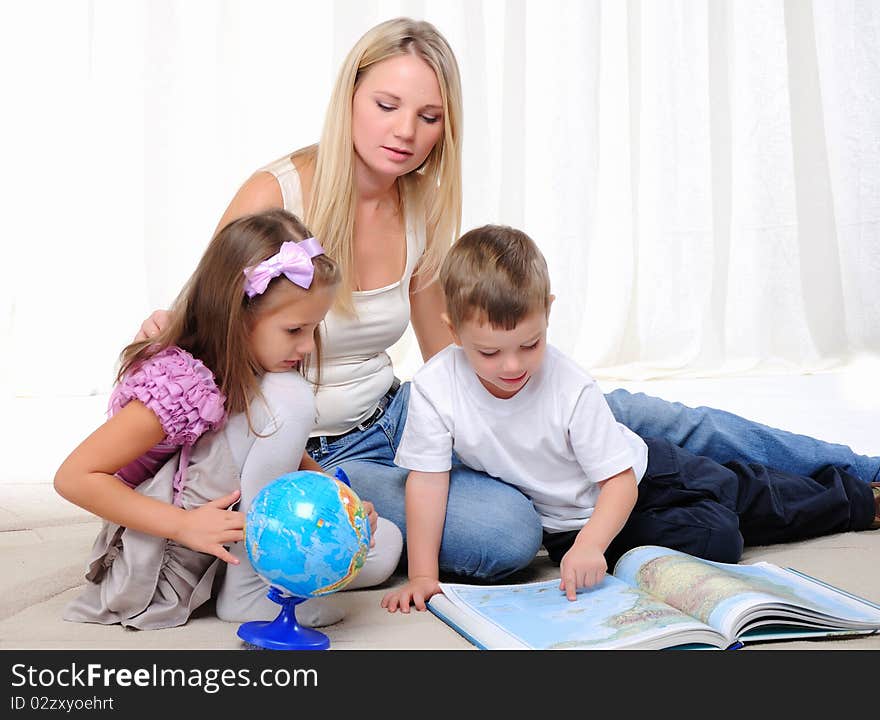 A young mother, her daughter and young son studying geography. Atlas and the globe.