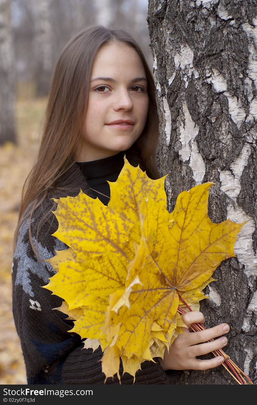 Portrait of cute girl in autumn park with leaves next to birch.