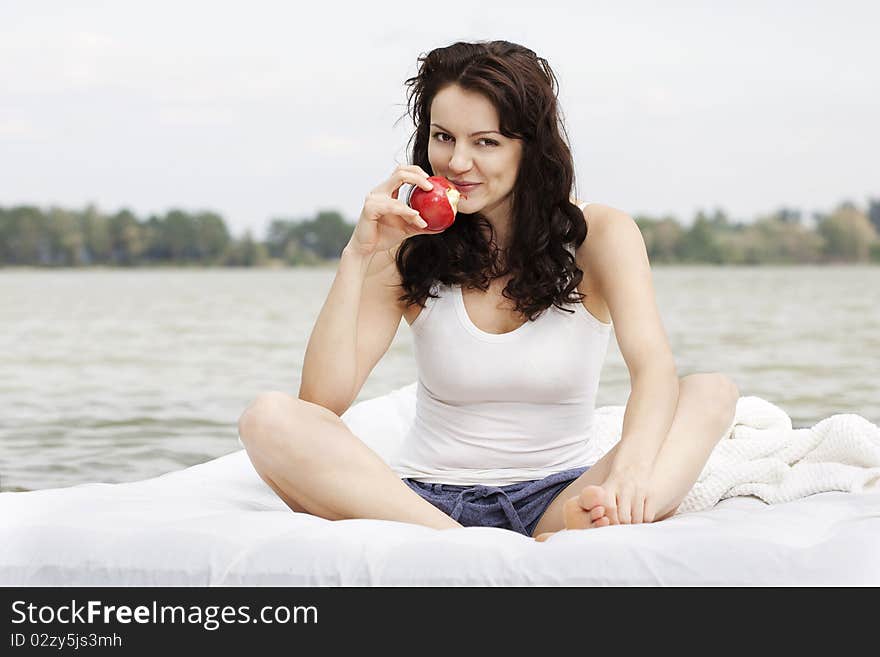 Beautiful young woman with apple lying on the white bed in the sea. Beautiful young woman with apple lying on the white bed in the sea