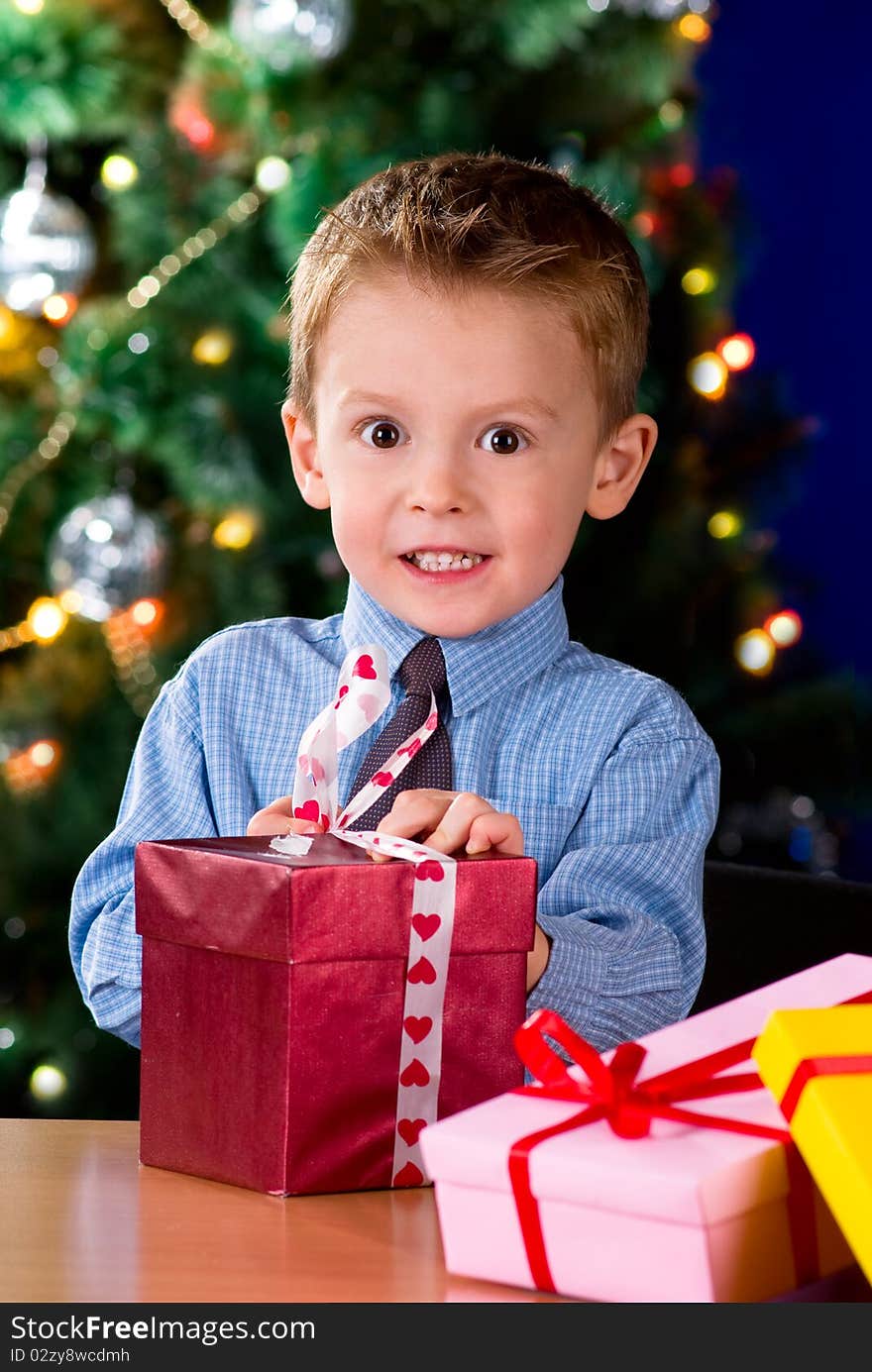 Happy little boy opening Christmas gifts near New Year's tree