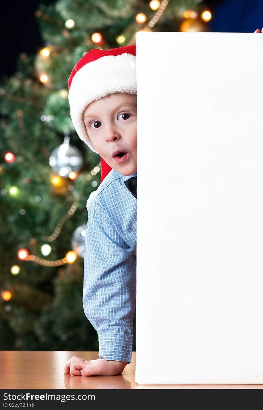 4 years old boy holding blank near New Year's tree with expression on his face. 4 years old boy holding blank near New Year's tree with expression on his face