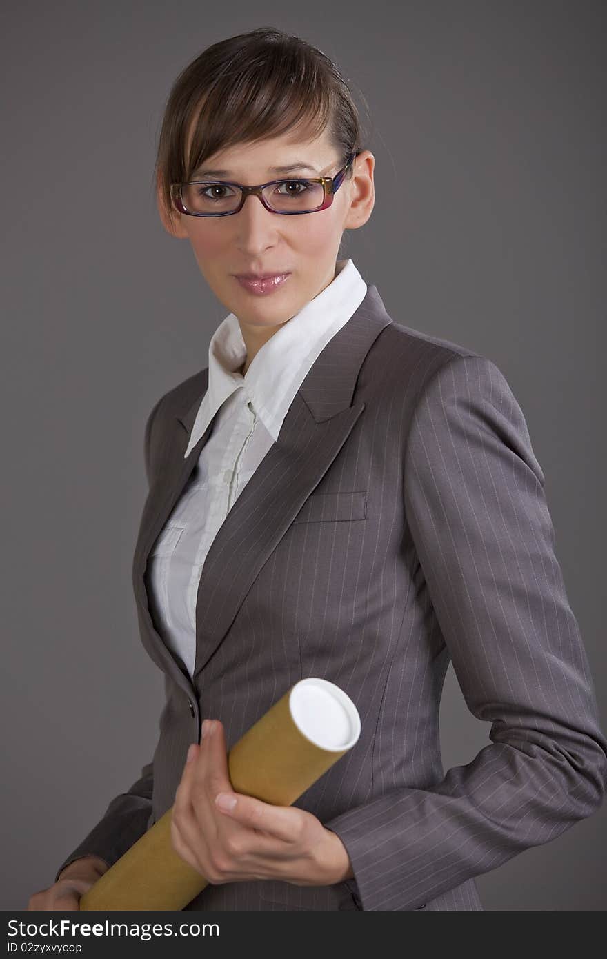 Portrait of business woman holding tube with blueprints over grey background. Portrait of business woman holding tube with blueprints over grey background