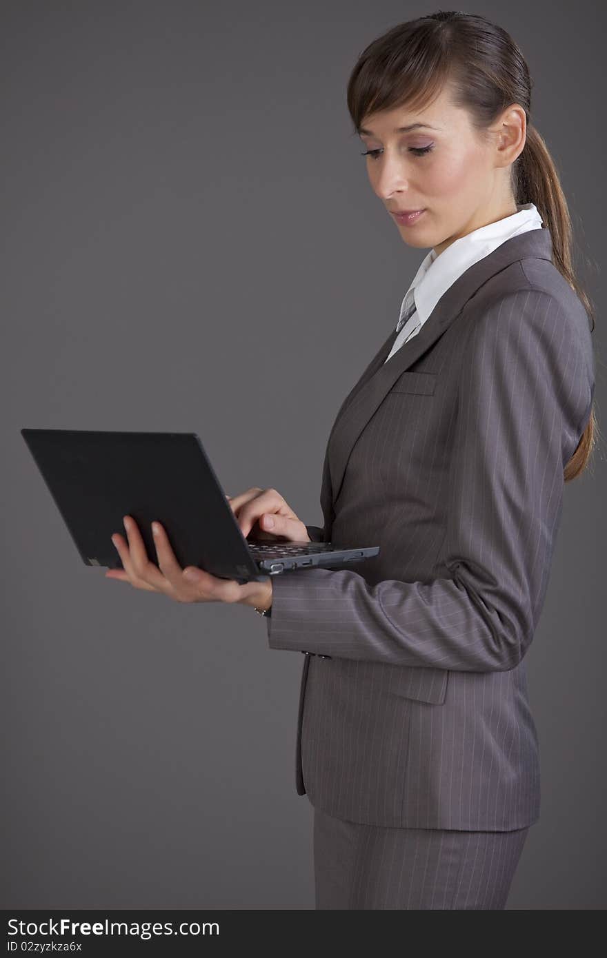 Portrait of business woman holding small computer over grey background. Portrait of business woman holding small computer over grey background