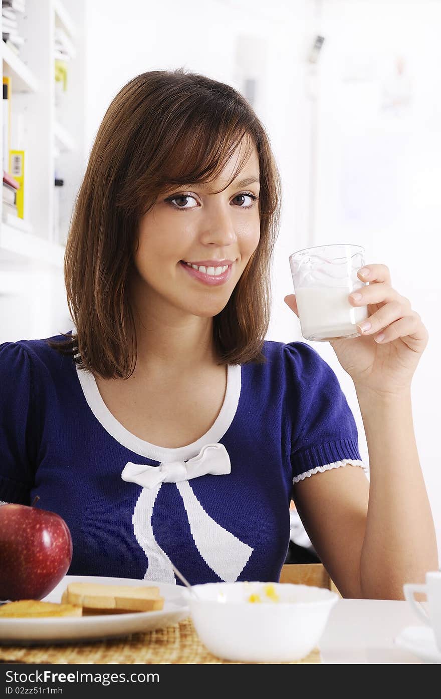 Young woman drinking milk on the white background, smiling and looking in camera