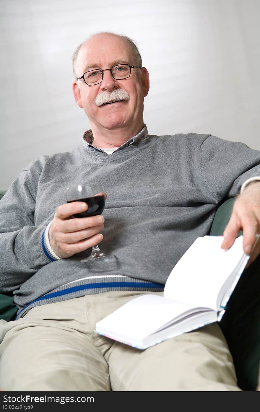 Senior man is reading a book with a glass wine