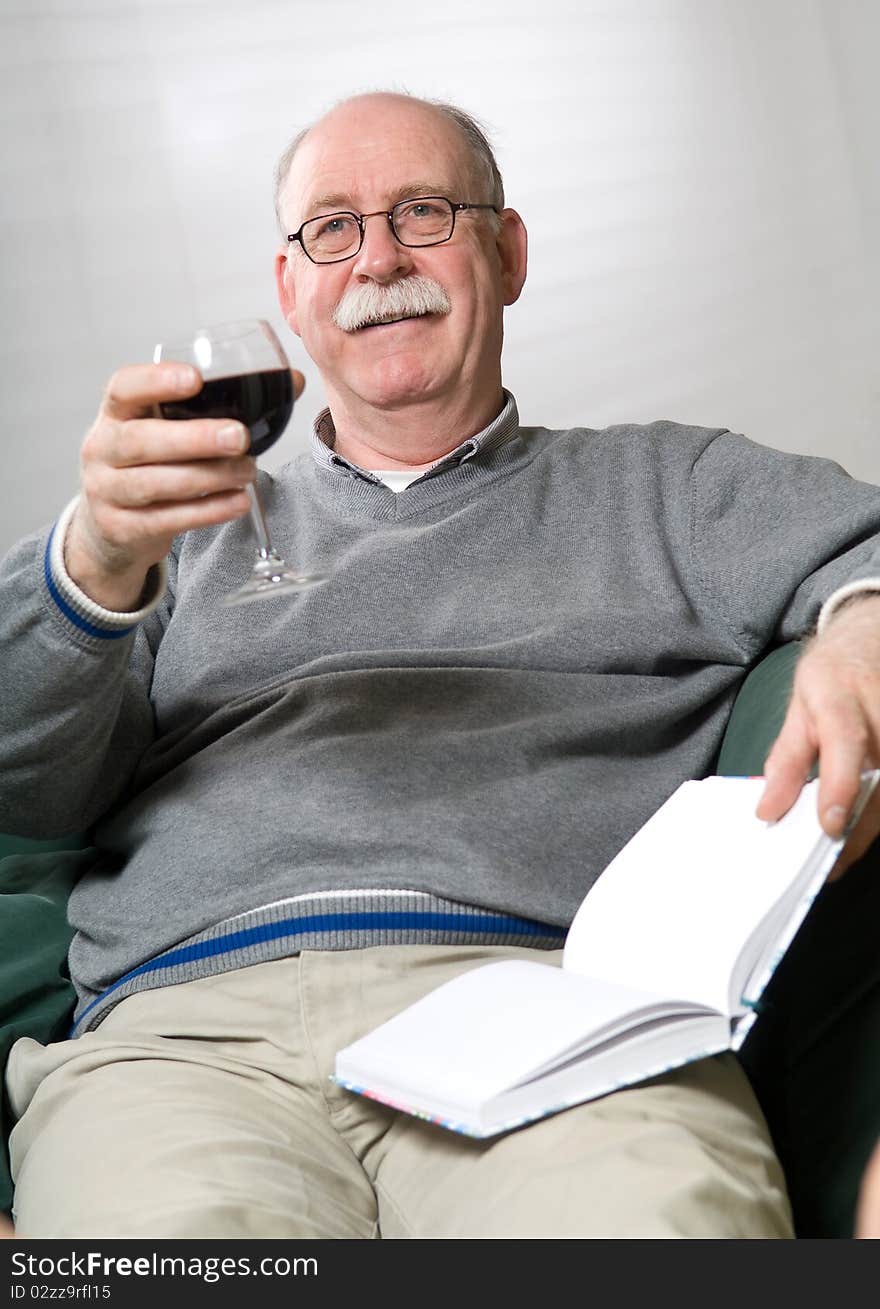 Senior man is reading a book with a glass wine