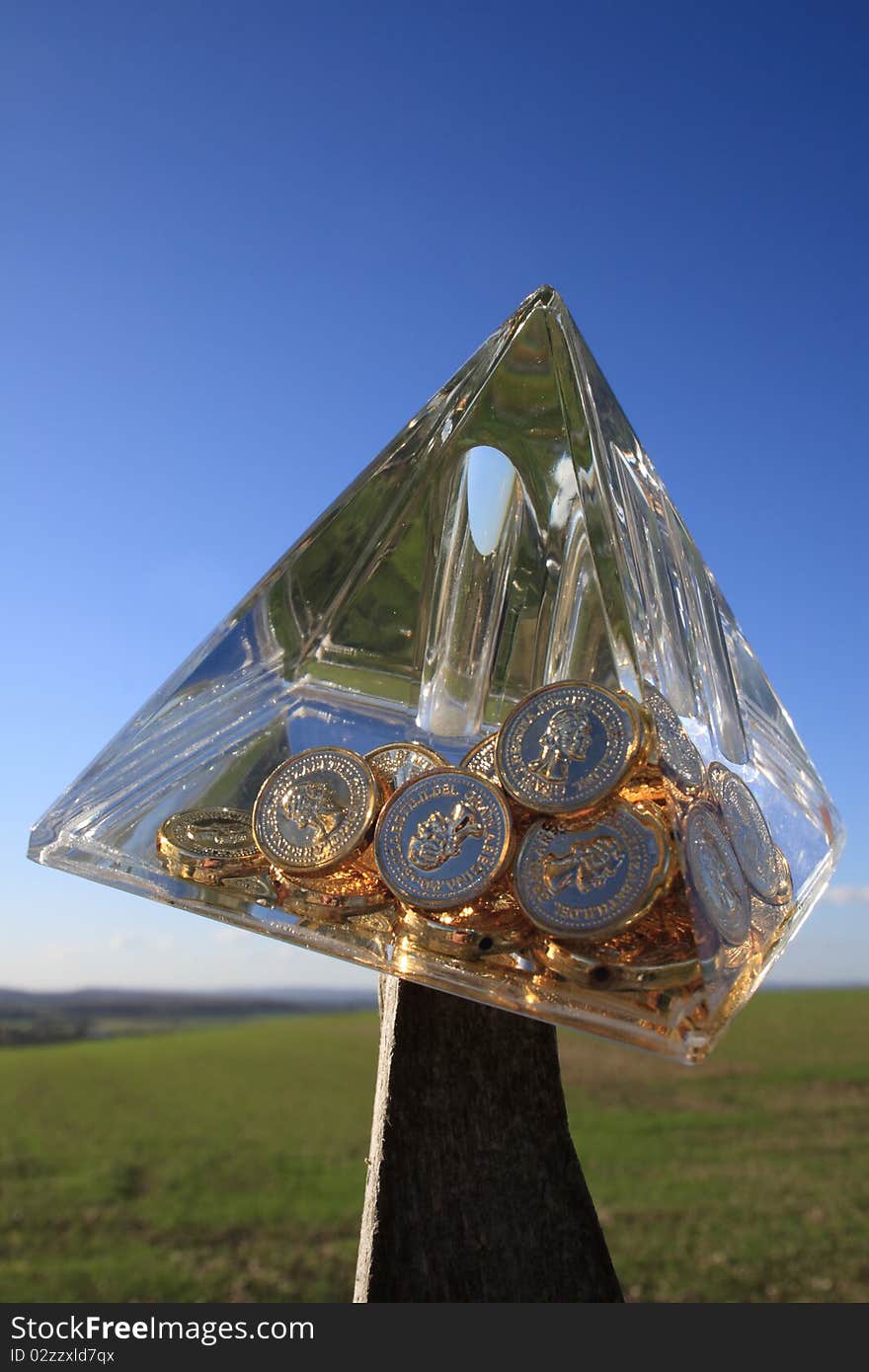 A Crystal Pyramid with gold coins inside toppling over and about to fall and crash. A Crystal Pyramid with gold coins inside toppling over and about to fall and crash.