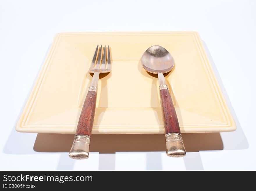 Orange square shaped plate with spoon and fork is placed on a white background. Orange square shaped plate with spoon and fork is placed on a white background.