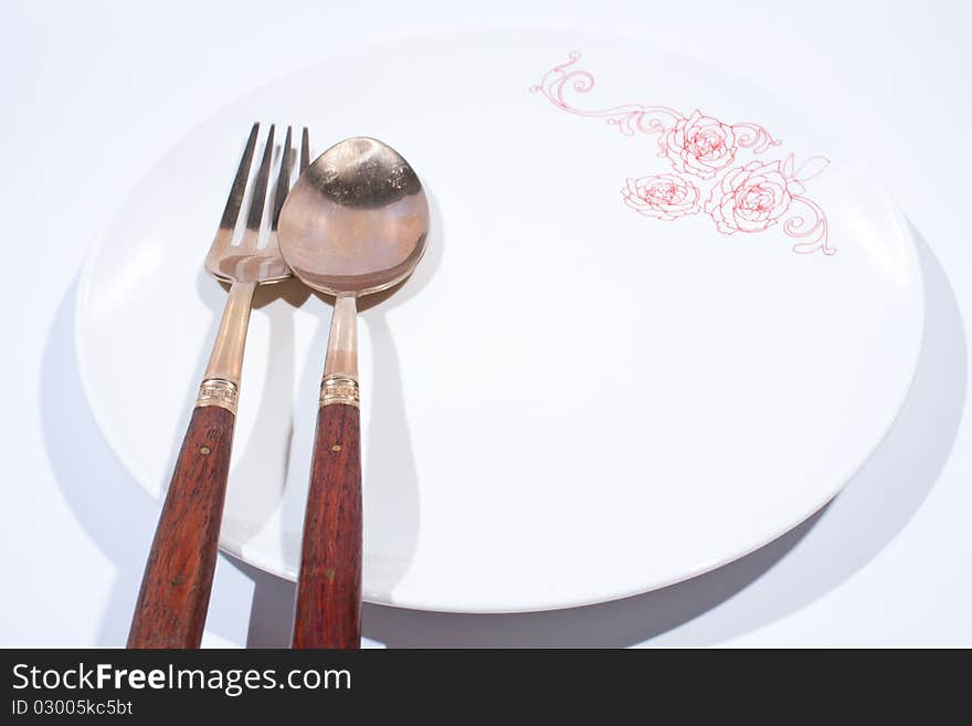 Round white plate with spoon and fork is placed on a white background. Round white plate with spoon and fork is placed on a white background.