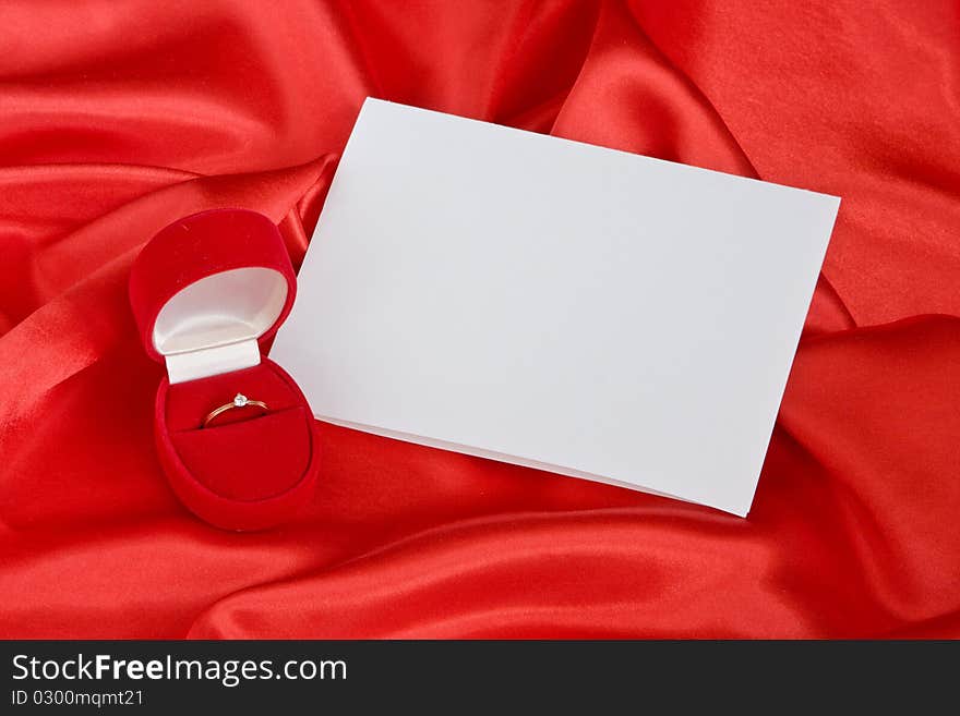 Golden ring in jewerly box and empty card on red satin