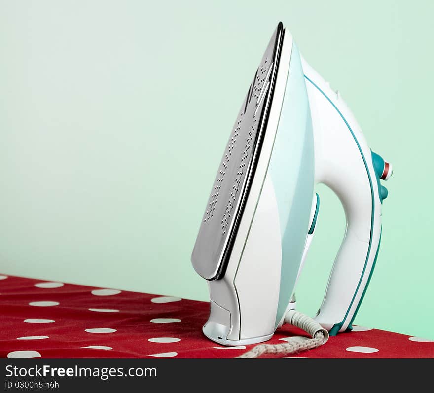 Modern electronic iron on an ironing board with green background