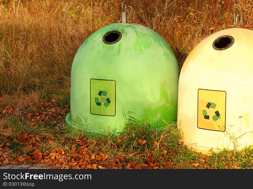 Two colorful recycling bins in a autumn park.