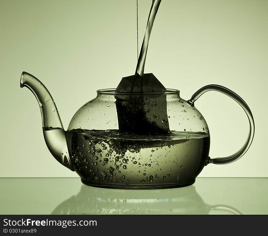 Water pouring into a teapot with a teabad in the pot. Green background. Water pouring into a teapot with a teabad in the pot. Green background.