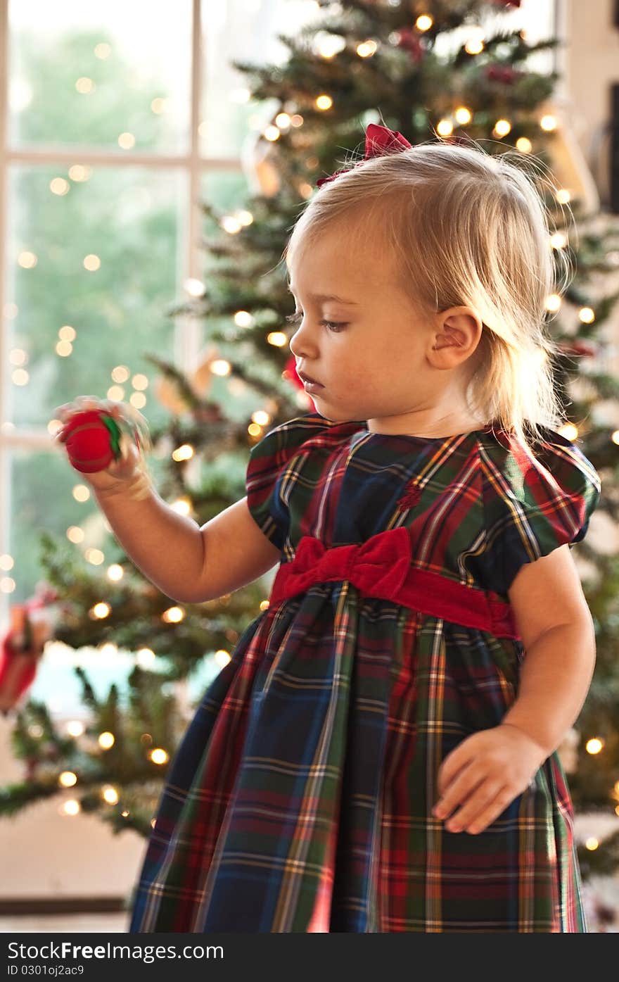 Little Girl Twisting an Ornament in front of a Christmas Tree. Little Girl Twisting an Ornament in front of a Christmas Tree