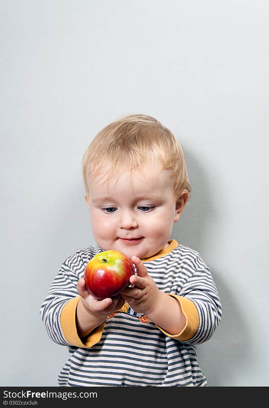 Charming baby with apple on a grey background