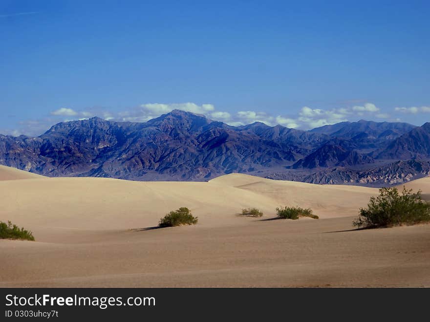 Beautiful, clear photo of Death Valley, California. Sand dunes brush up agains purple mountains with puffy clouds peeking over them. Beautiful, clear photo of Death Valley, California. Sand dunes brush up agains purple mountains with puffy clouds peeking over them.