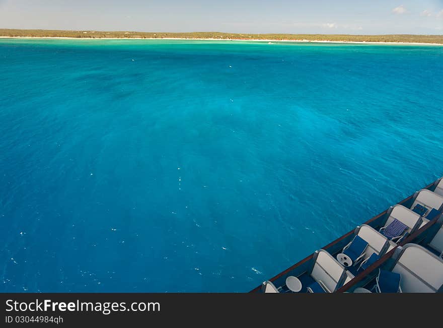 Caribbean island view from cruise ship deck. Contains intense blue water, island and part of cruise ship decks.