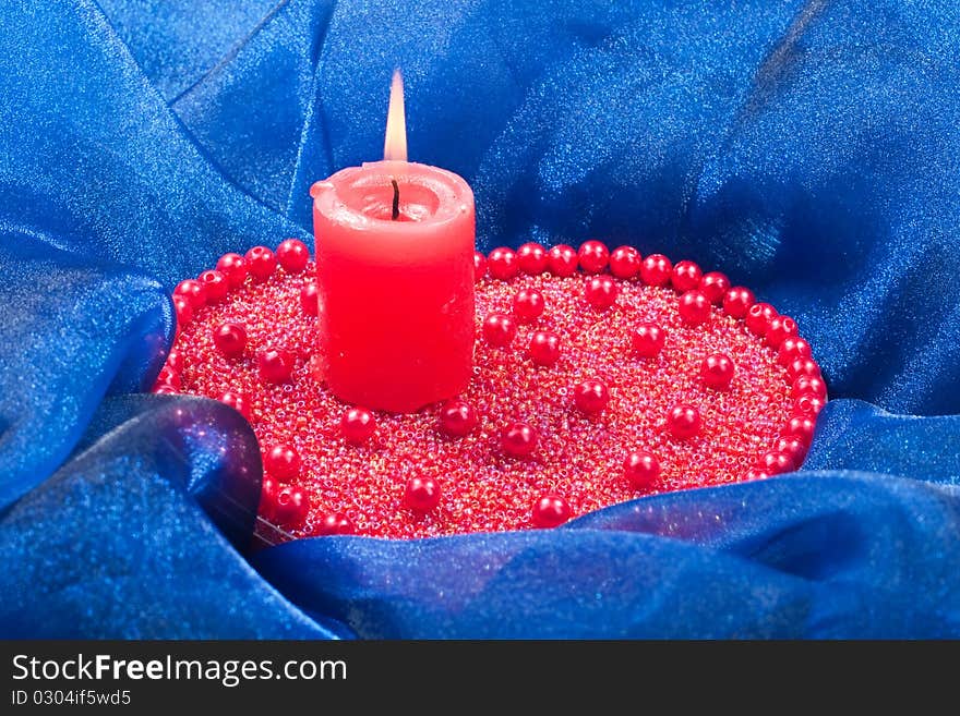 Burning candle with red ribbon placed on beads. Burning candle with red ribbon placed on beads