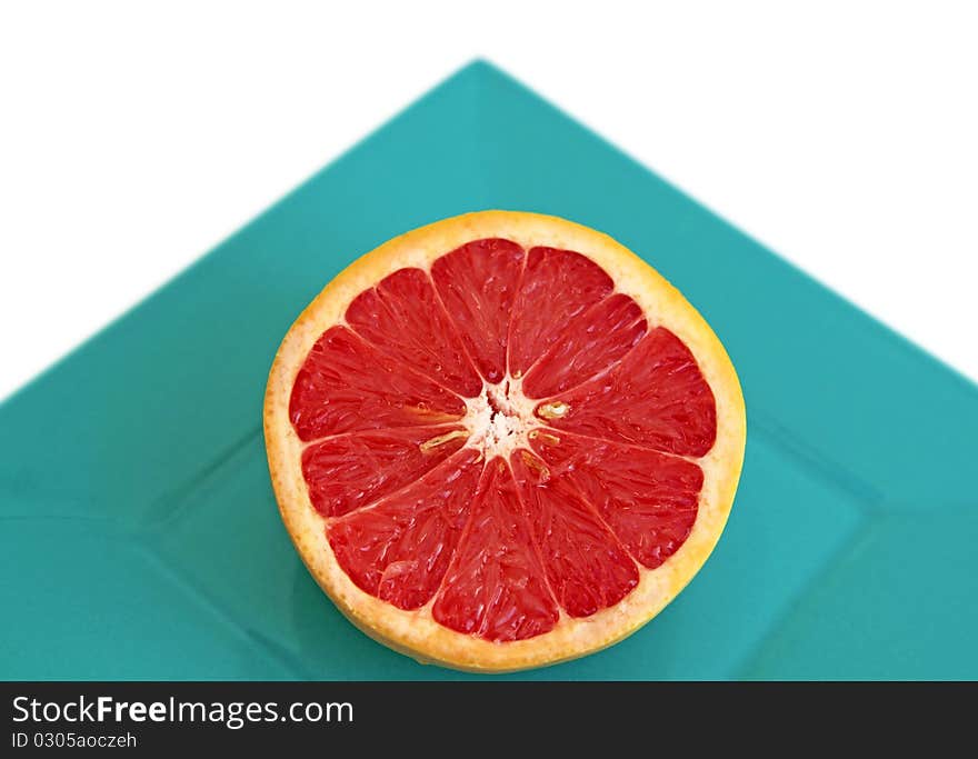 Half a red grapefruit in a square plate shot on white background with angle showing simple geometrical shapes. Half a red grapefruit in a square plate shot on white background with angle showing simple geometrical shapes.