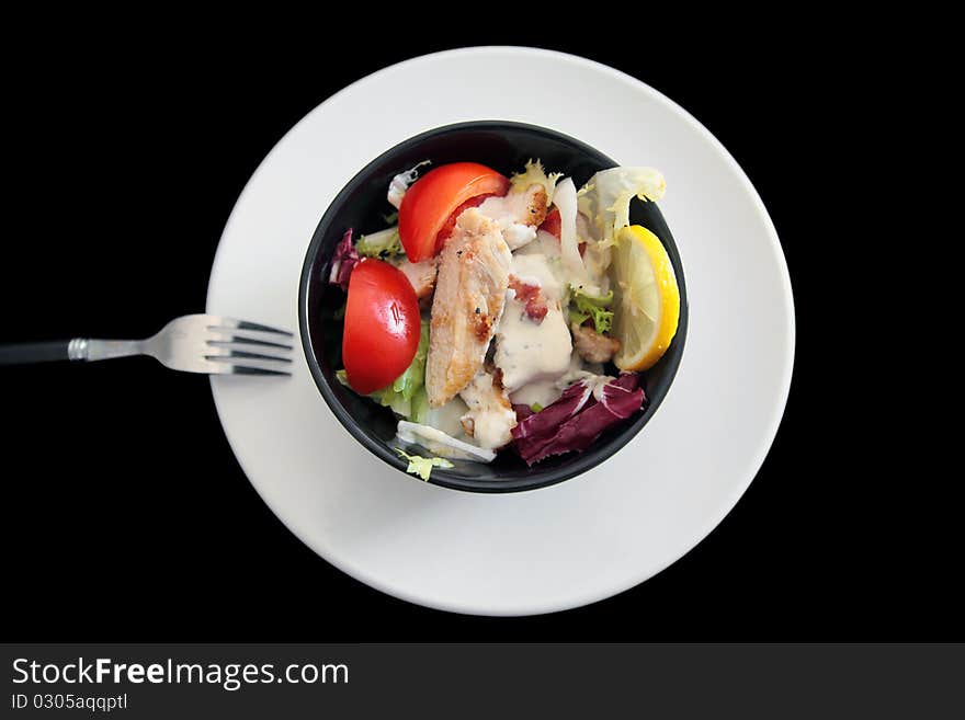 Portion of a mixed salad with chicken, tomatoes, various lettuce, bacon bits, lemon, Caesar sauce - shot on black background. Portion of a mixed salad with chicken, tomatoes, various lettuce, bacon bits, lemon, Caesar sauce - shot on black background.