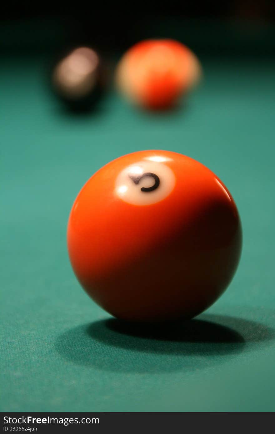 Orange billiard ball which lies on a green table has been photographed up close.