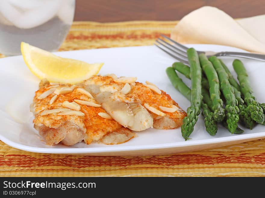 Fish fillets topped with crab meat sauce and almond slivers with asparagus and slice of lemon. Fish fillets topped with crab meat sauce and almond slivers with asparagus and slice of lemon