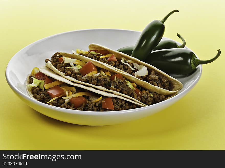 Taco wrap with beef meat in a white plate. Green hot pepper on the side. Yellow background. Taco wrap with beef meat in a white plate. Green hot pepper on the side. Yellow background.