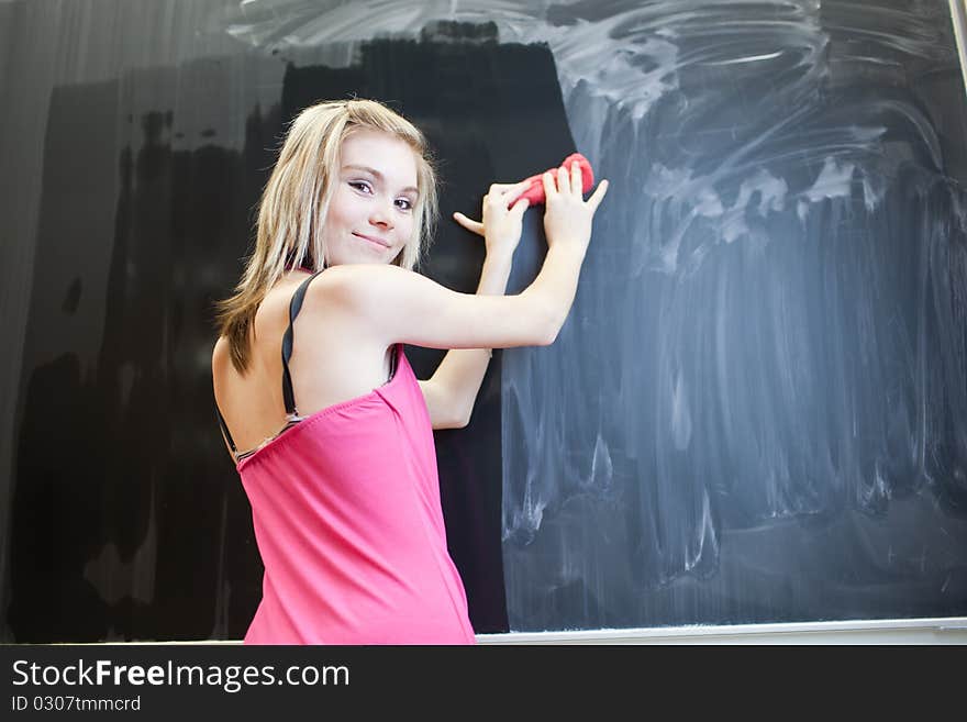 Pretty young college student erasing the chalkboard/blackboard during a math class (color toned image)