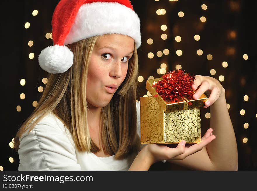 Teen girl wearing a Santa hat holds a golden wrapped gift. Teen girl wearing a Santa hat holds a golden wrapped gift.