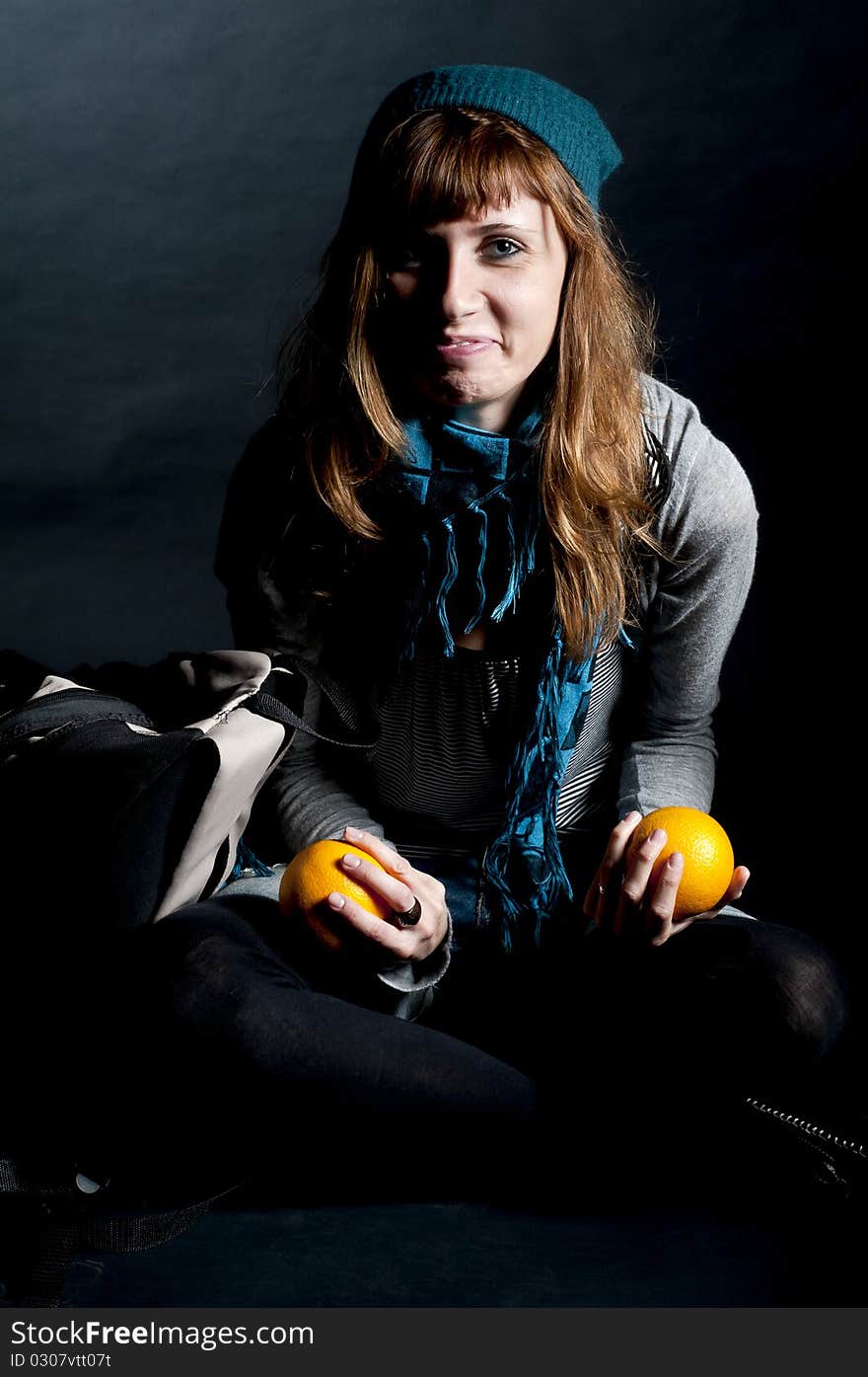 Beautiful girl with scarf and hat and oranges on a black background