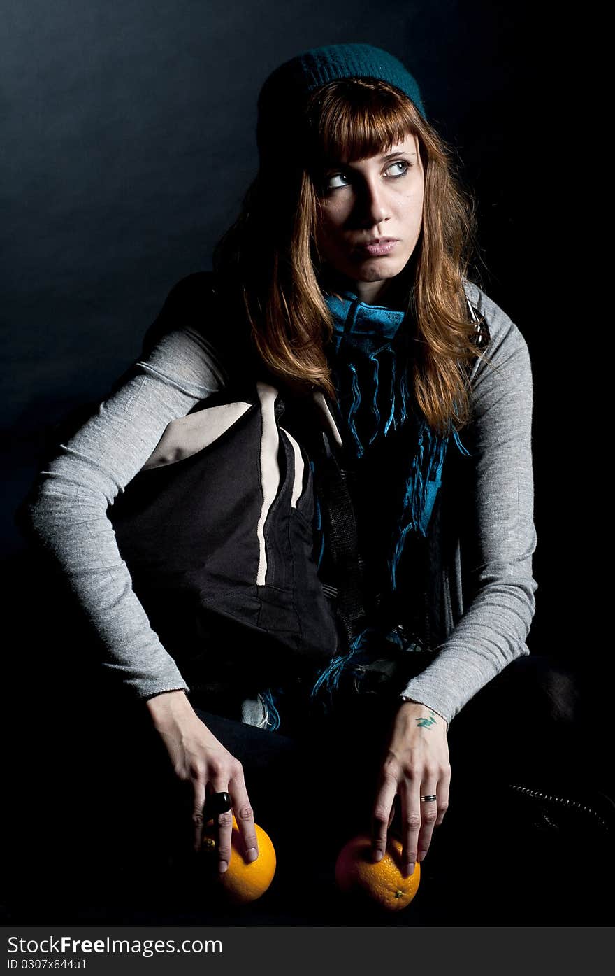 Beautiful girl with scarf and hat and oranges on a black background