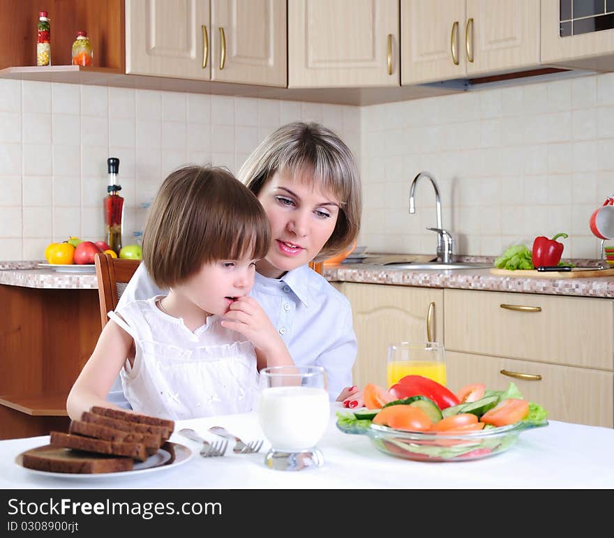 Mama and her little daughter eating breakfast in the morning together in the kitchen.