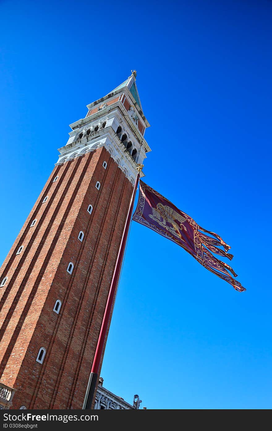 Campanile and Venetian flag against clear, blue sky. Venice, Italy.