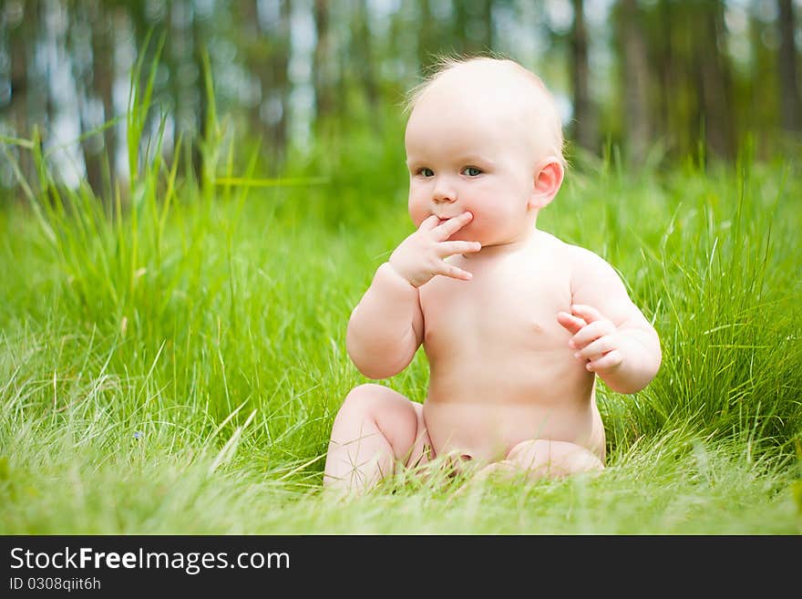 Baby sitting on green grass with fingers in mouth