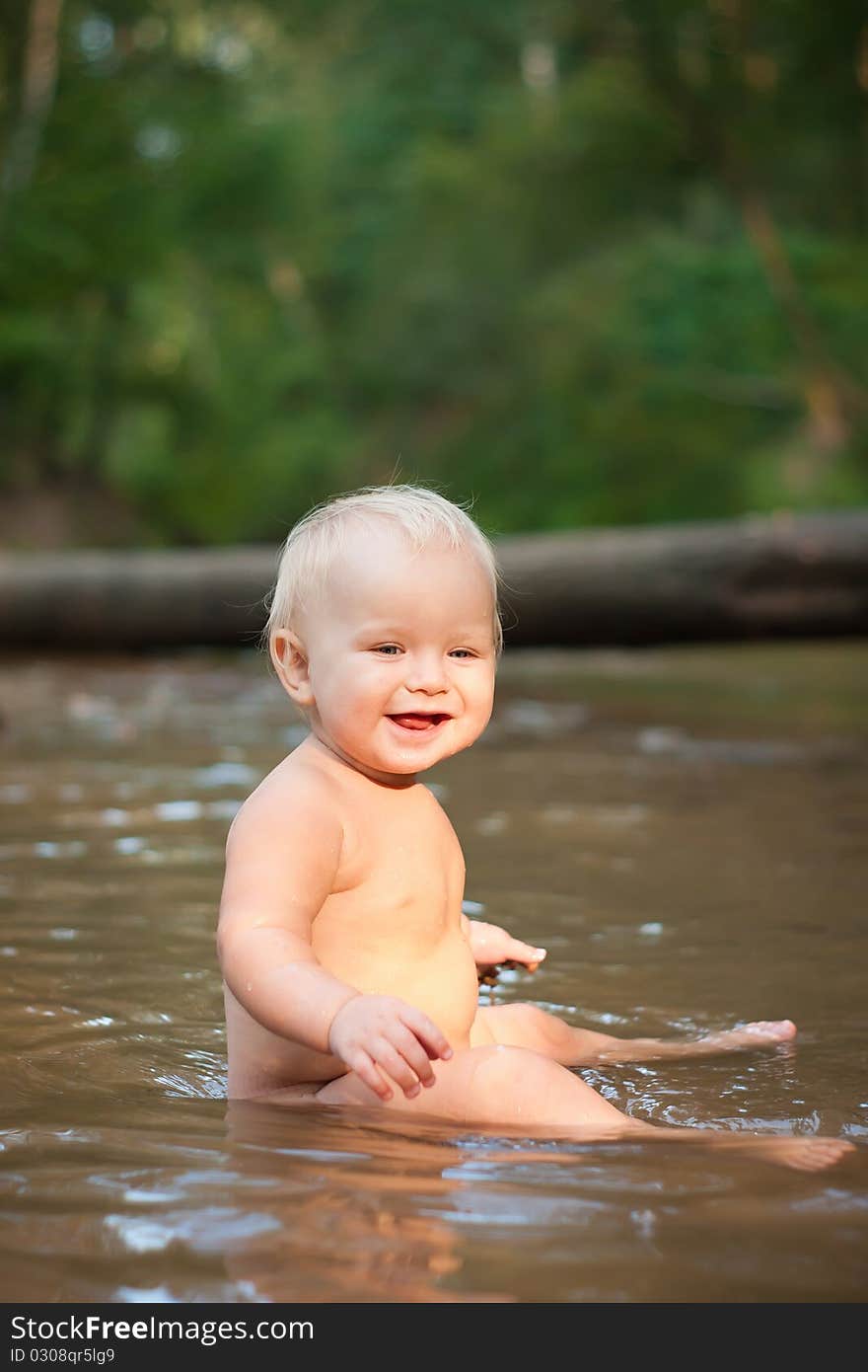 Little girl sitting in the river water on sunset.