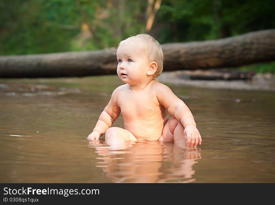 Little girl sitting in the river water on sunset