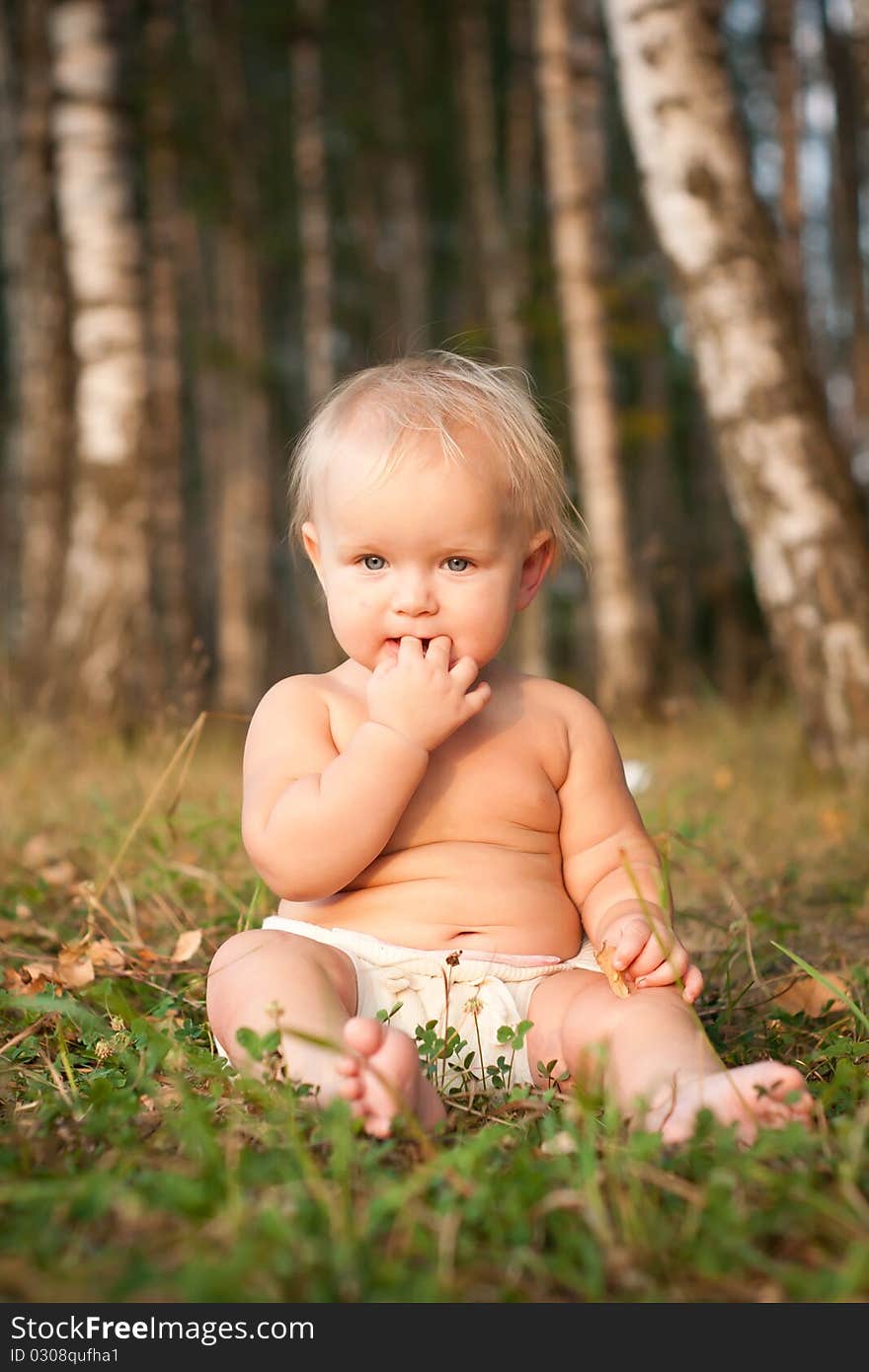 A little girl sitting on green grass in the park near forest.