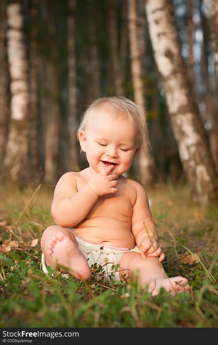 A little girl sitting on green grass in the park near forest