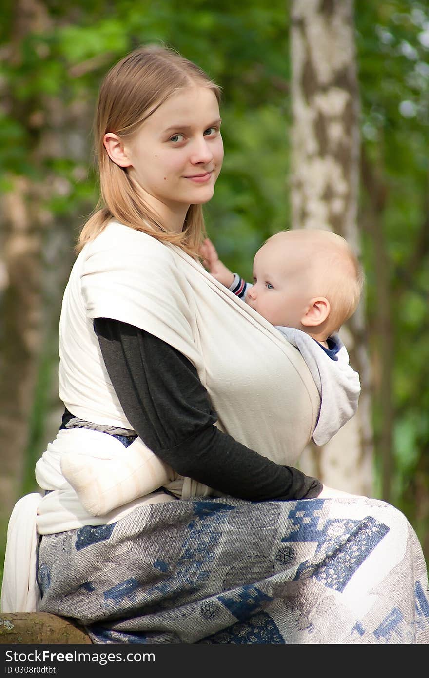 Mother sit  with daughter in sling in park. Mother sit  with daughter in sling in park.