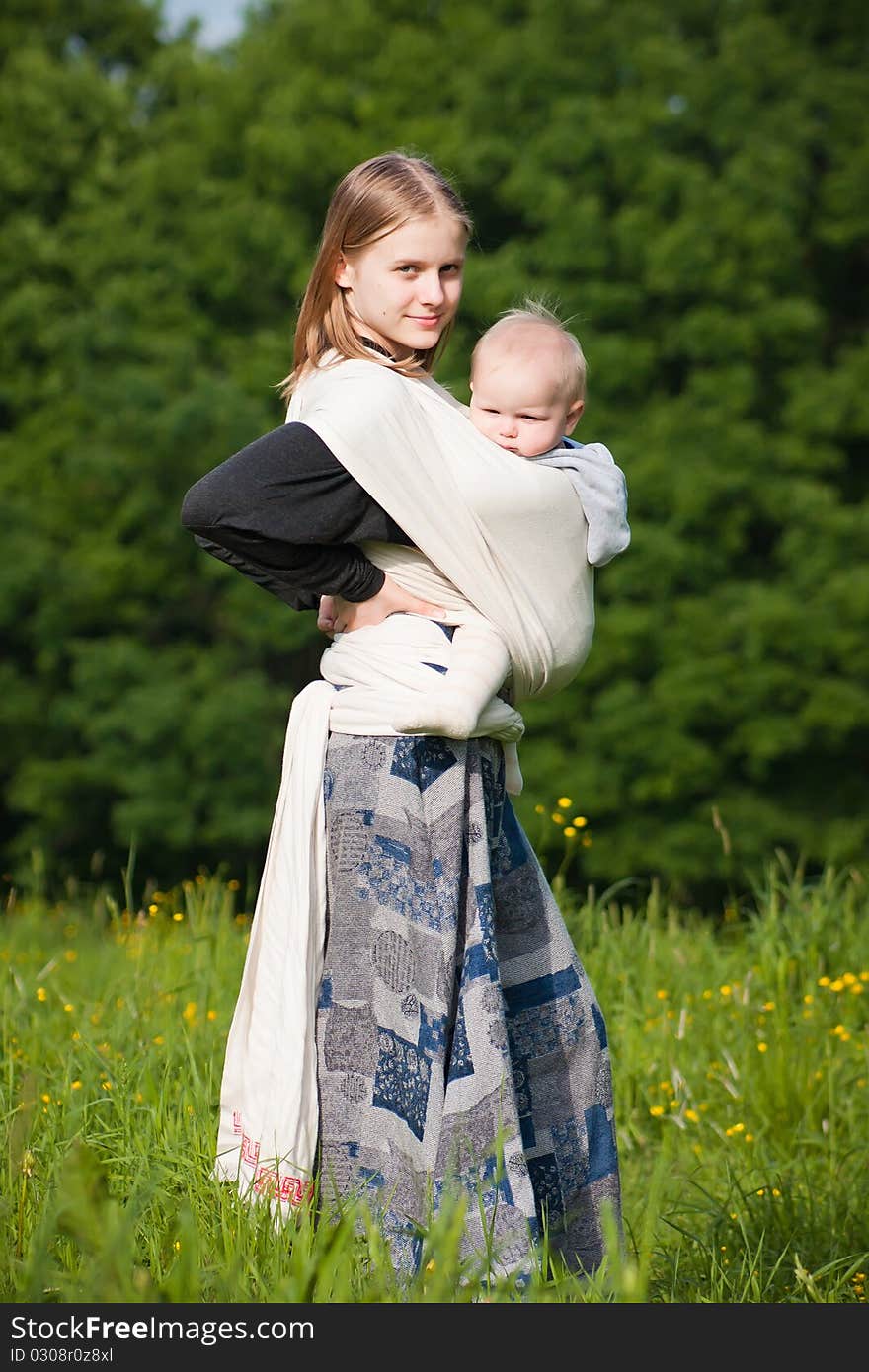 Mother carrying daughter in sling in park.