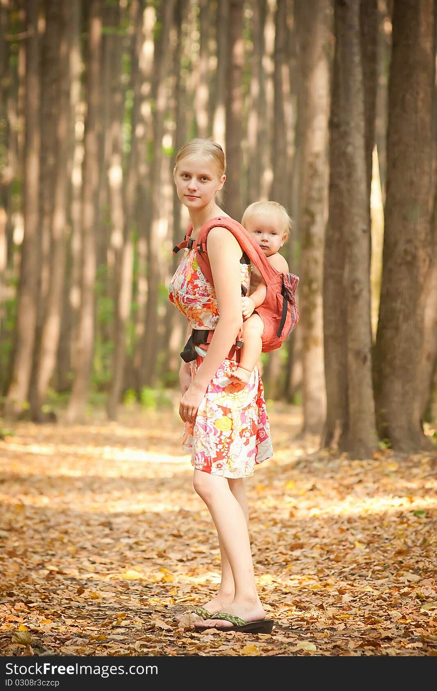 Mother carrying daughter in sling in forest.