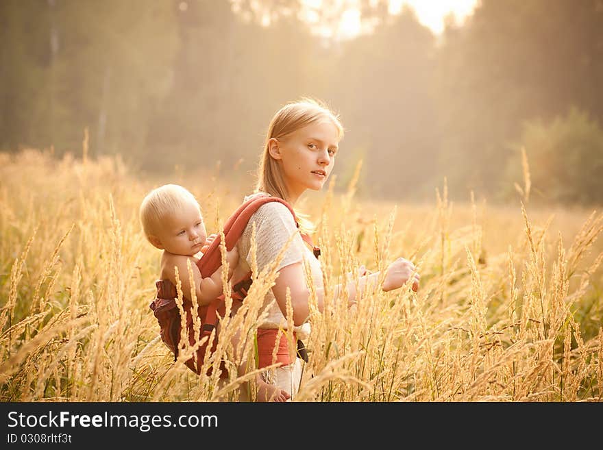 Mother and daughter walking near forest by the road in the wheat field on sunset.