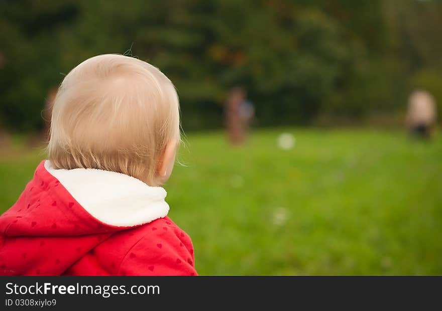 Young adorable baby stay on grass in park watching ball game. Young adorable baby stay on grass in park watching ball game